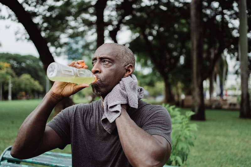 Black man drinking juice while wiping sweat off his neck after exercise