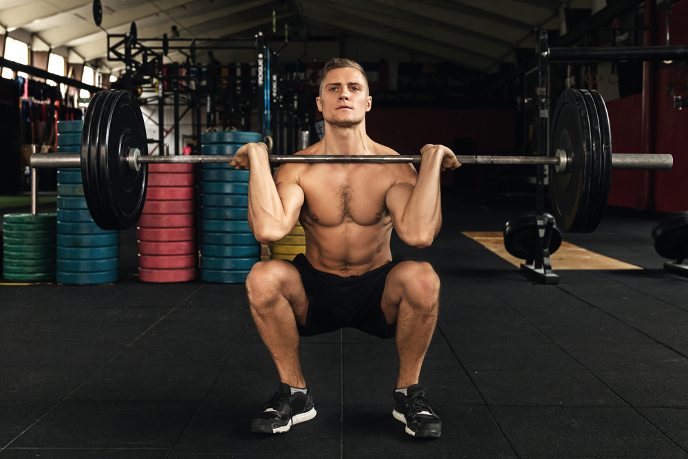 Topless man doing a front squat in a gym