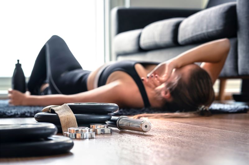 A woman lying on the floor after exercise resting her arm on her head and holding a bottle of water