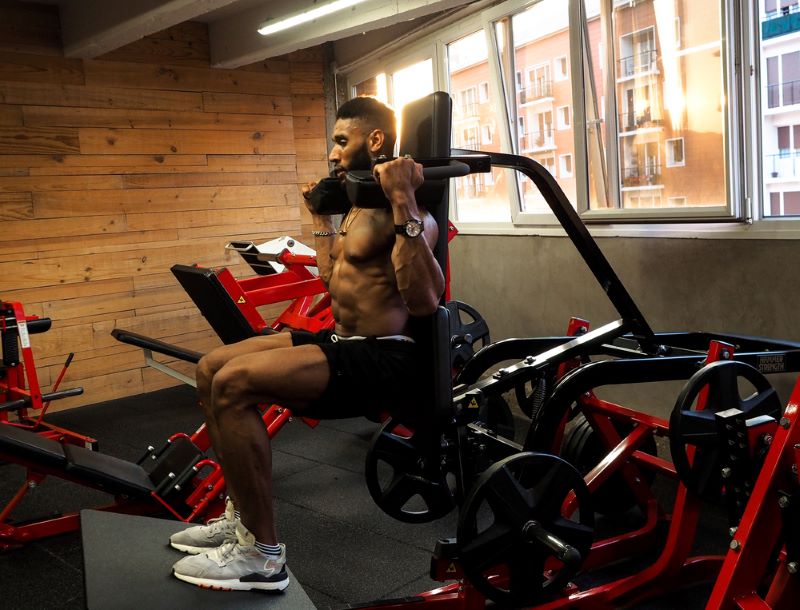 Topless man doing a hack squat in a gym on leg day