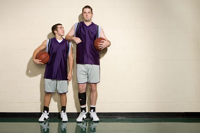 tall basketball player stood next to a small basketball plater