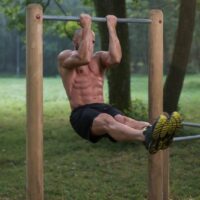 Topless man doing chin-ups outside