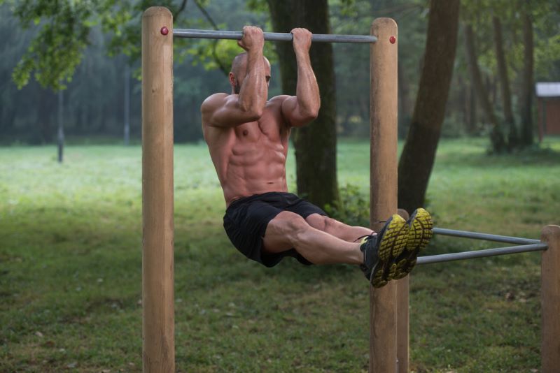 Topless man performing a chin-up in a park