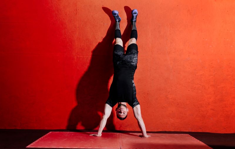 Man doing a handstand push-up on a carpet in front of a red wall