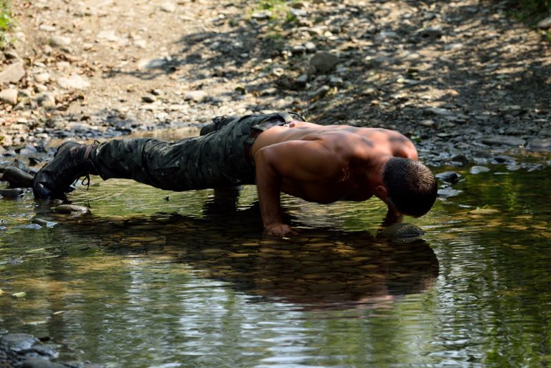 Topless man doing a military push-up in a river