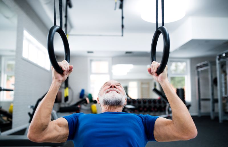 Old man doing a ring pull-up in a gym