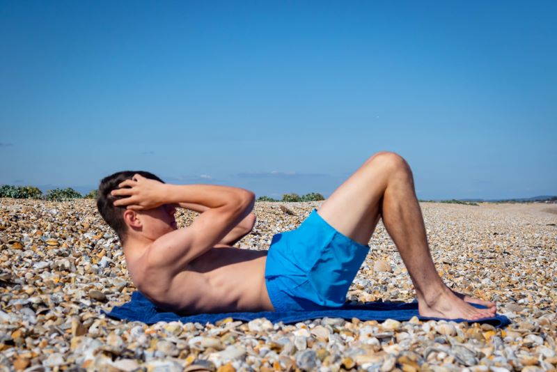 Young boy doing a sit-up on a towel on a beach